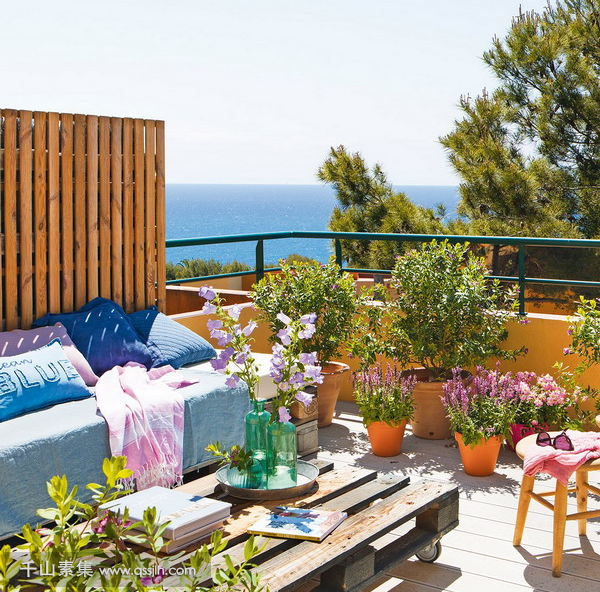 06-The-terrace-is-decorated-with-some-stools-a-pallet-table-a-daybed-and-lots-of-potted-flowers-and-greenery.png